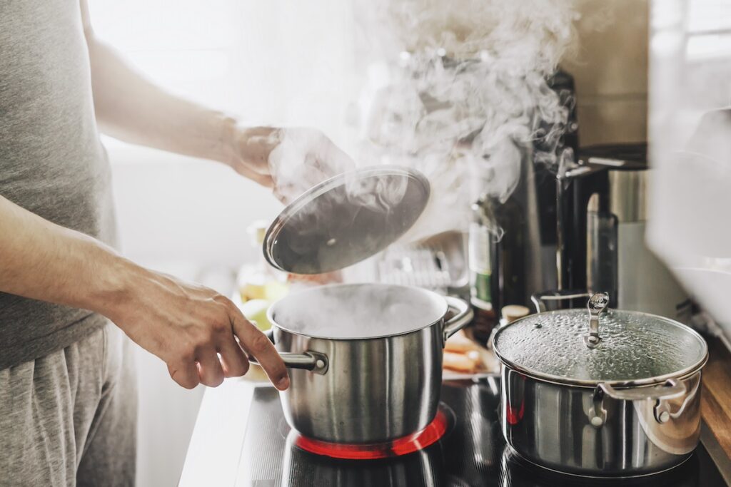 young man cooking fresh food home opening lid steaming pot